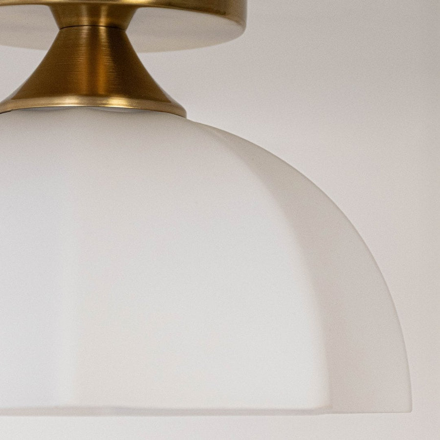 Closeup of gold metal ceiling mount with white glass shade showing refined craftsmanship clean edges and smooth detailing.
