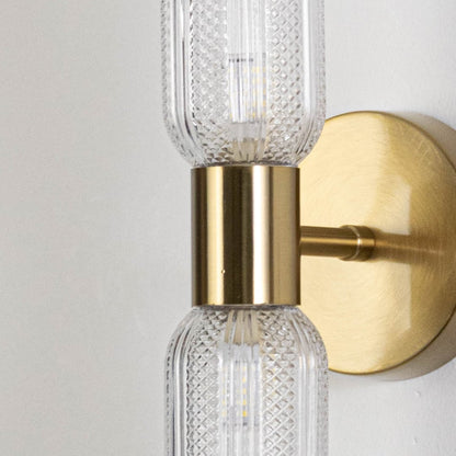 Closeup of modern gold wall sconce with dual textured glass tube shades and round metal base showing elegant craftsmanship details.