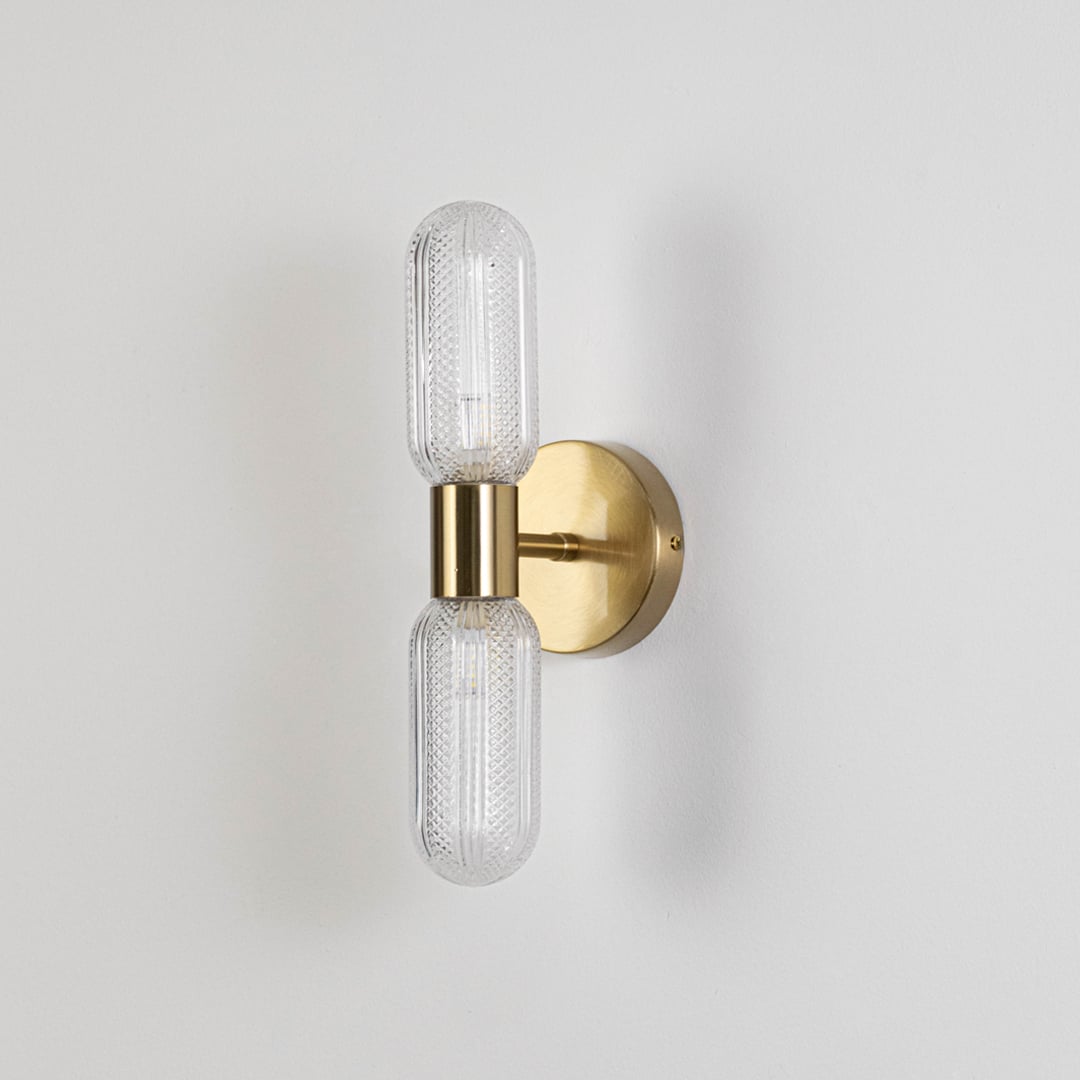 Minimalist gold wall sconce with dual textured glass tube shades switched off displayed on plain white background for product display.
