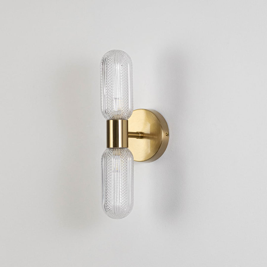 Minimalist gold wall sconce with dual textured glass tube shades switched off displayed on plain white background for product display.