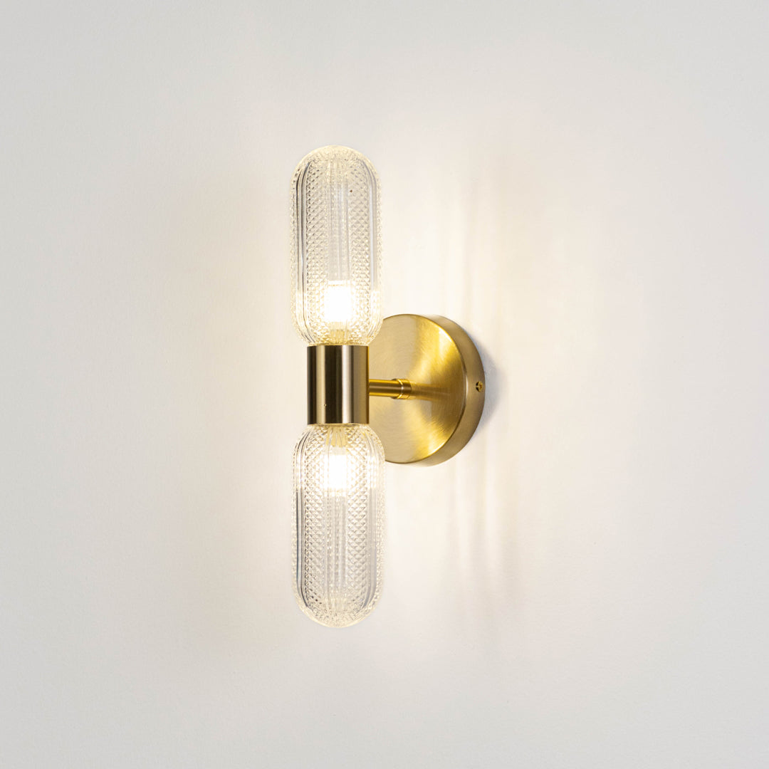 Contemporary wall light in gold metal finish with dual glass tube shades for bedroom or living decor lighting white background.