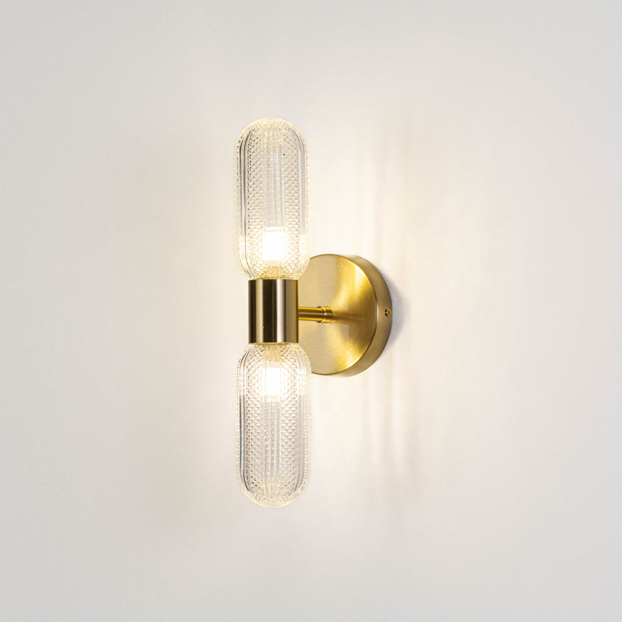Contemporary wall light in gold metal finish with dual glass tube shades for bedroom or living decor lighting white background.