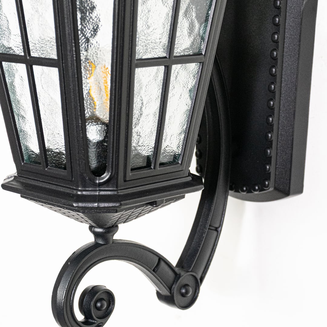 Closeup view of black metal wall lantern highlighting textured glass panels roof detailing and solid outdoor construction.