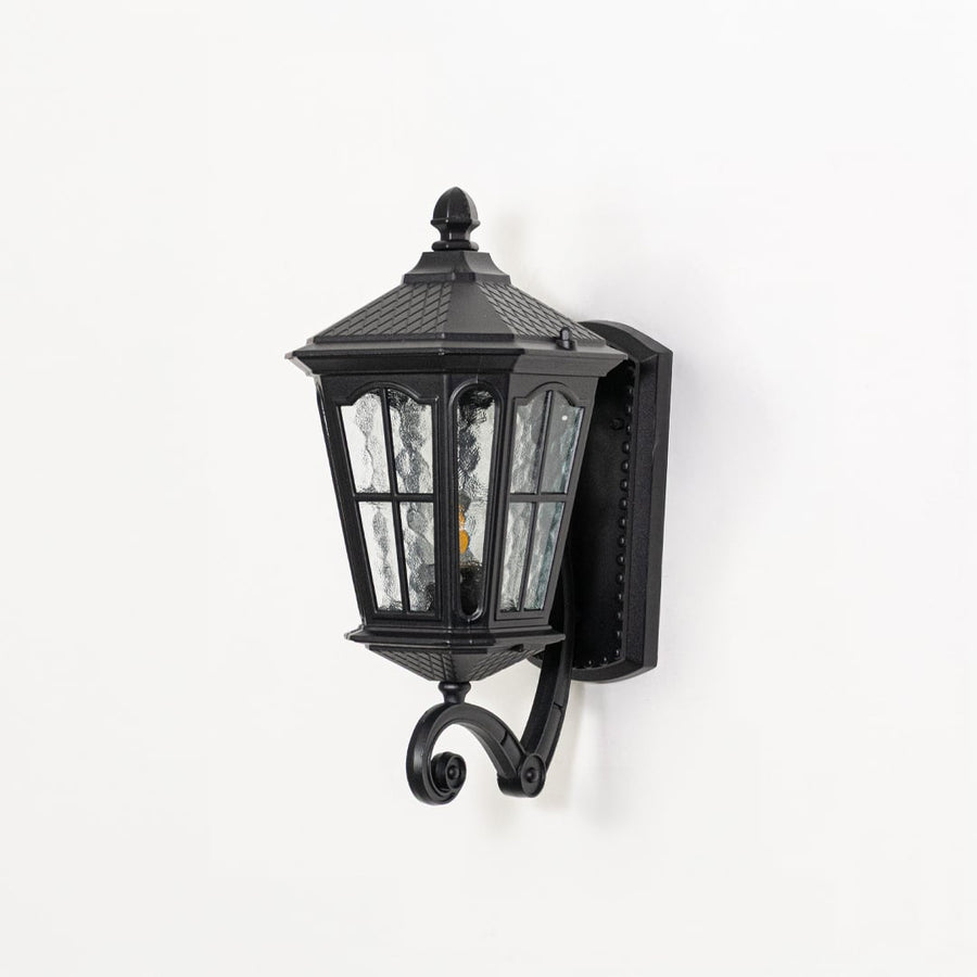 Outdoor wall lantern in black metal switched off on white background highlighting textured glass panels and classic lantern form.