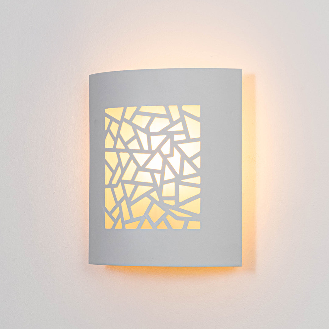 White metal wall light glowing warmly on white wall with geometric cutout design for modern decor.