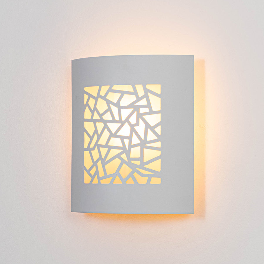White metal wall light glowing warmly on white wall with geometric cutout design for modern decor.