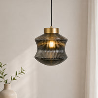 Contemporary gold brass pendant light with a vertical ribbed hourglass translucent smoke glass shade hanging in a room corner.