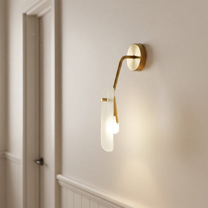Luxury gold wall lamp with an artistic frosted glass panel diffuser illuminating a modern white hallway entry corner.