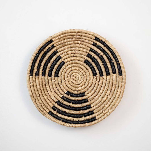 Handwoven seagrass round wall basket decor in natural beige and black with spiral woven pattern displayed on white background.