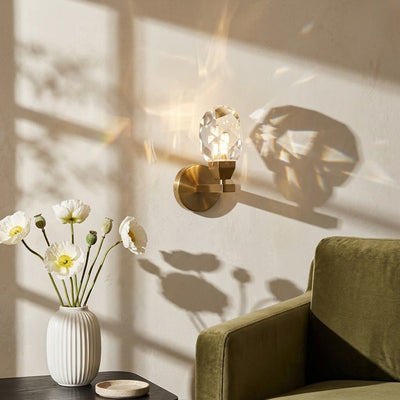 Luxury crystal globe wall sconce with a gold brass base casting artistic geometric shadows onto a living room wall next to an armchair.