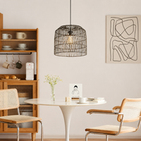 A black metal wire cage pendant light hangs over a white dining table in a modern, minimalist dining room with wooden chairs and a wooden shelving unit.