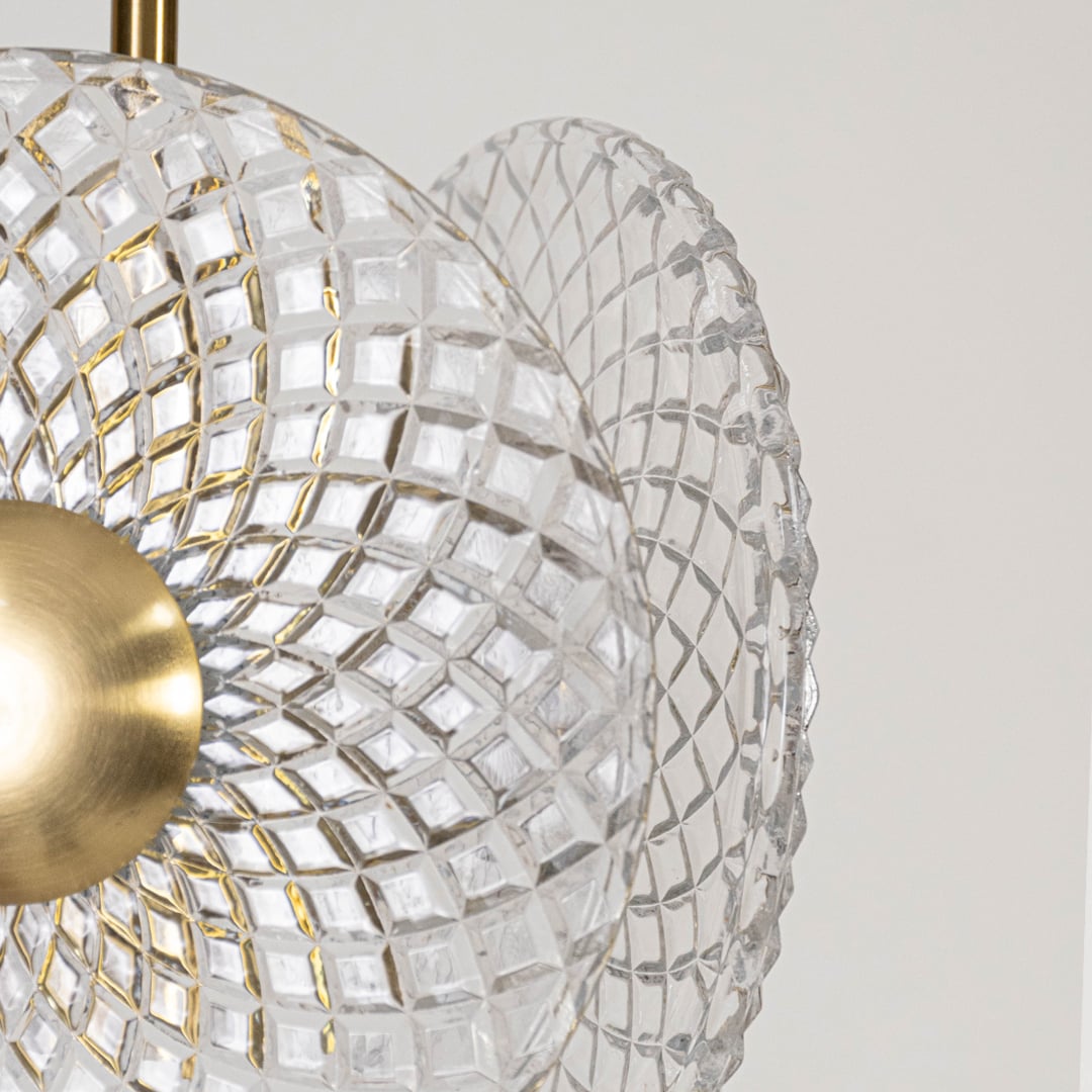 Closeup of luxury crystal pendant light with textured glass discs and golden metal finish for modern interior decor.