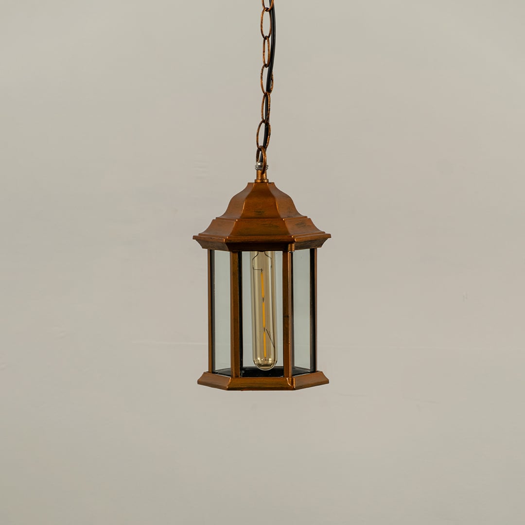 Copper metal hanging lantern on white background with light off showing clean hexagonal frame clear glass panels and traditional design suited for outdoor ceilings.