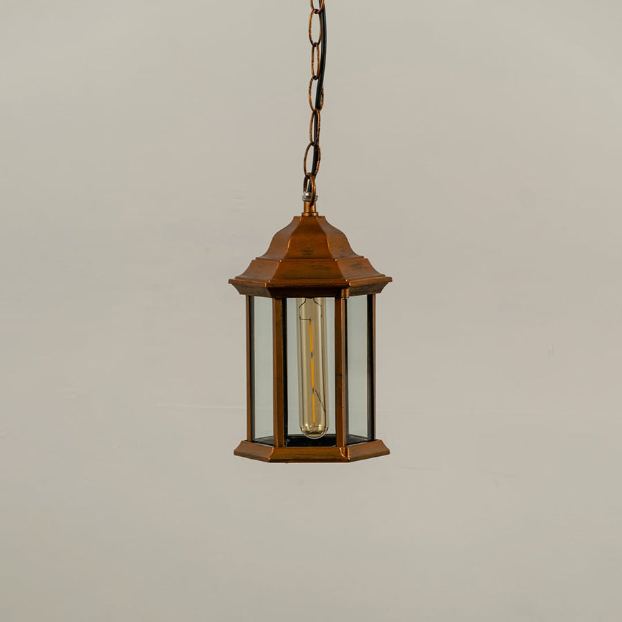 Copper metal hanging lantern on white background with light off showing clean hexagonal frame clear glass panels and traditional design suited for outdoor ceilings.