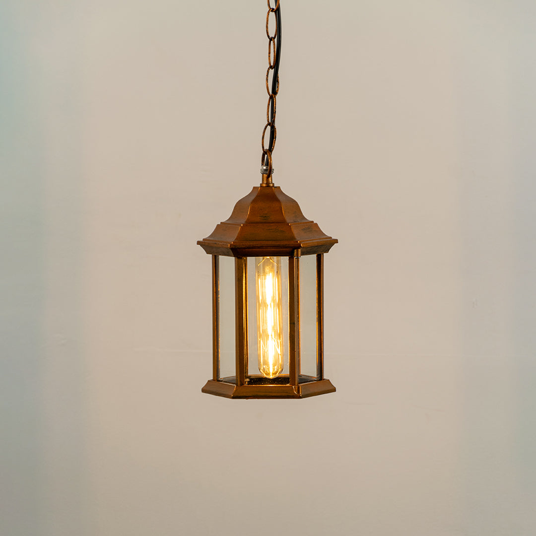 Copper metal hanging outdoor lantern with glass enclosure glowing on white background suitable for porch entrance and exterior decor lighting.