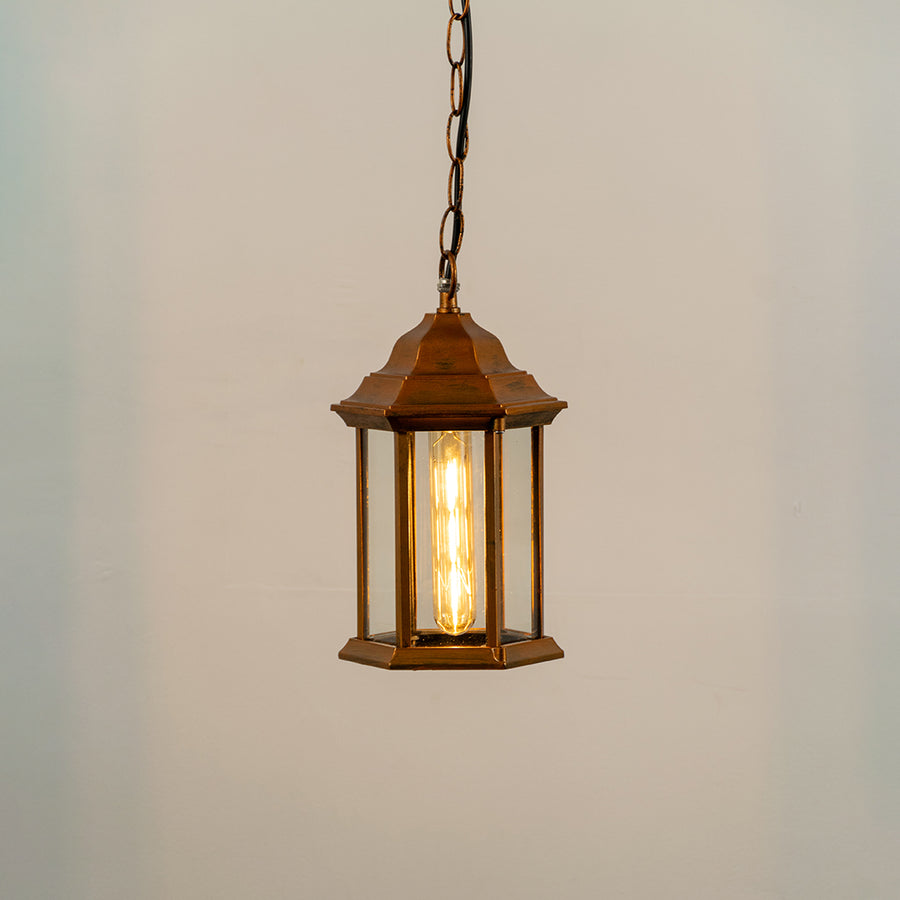 Copper metal hanging outdoor lantern with glass enclosure glowing on white background suitable for porch entrance and exterior decor lighting.