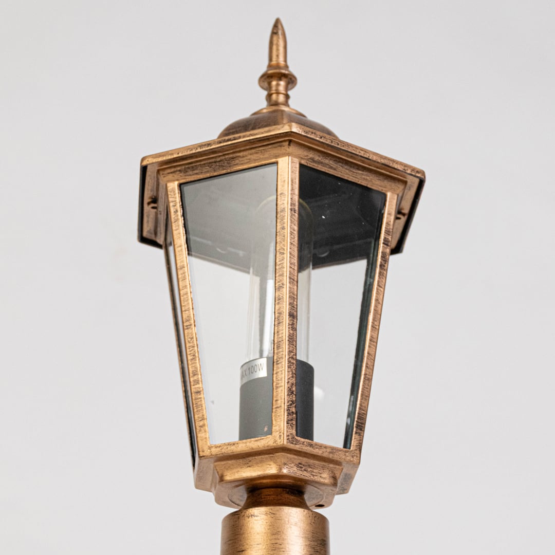 Closeup of antique gold outdoor lantern showing tapered glass panels metal frame detailing and classic exterior lighting design.