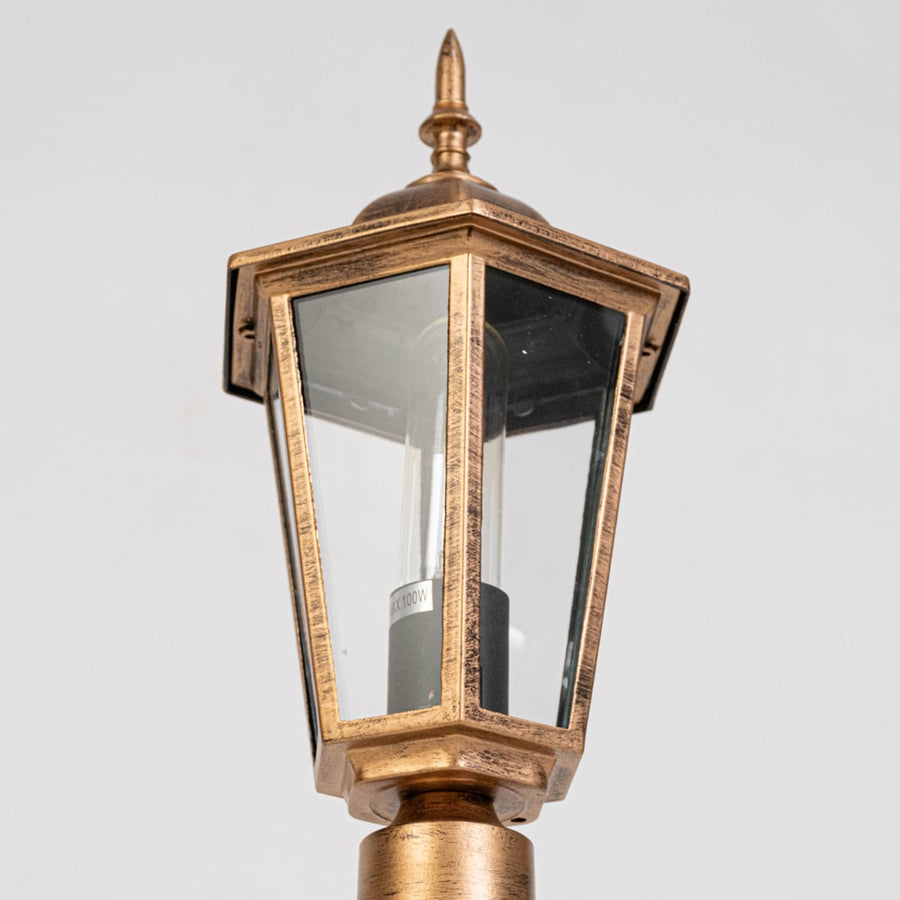 Closeup of antique gold outdoor lantern showing tapered glass panels metal frame detailing and classic exterior lighting design.