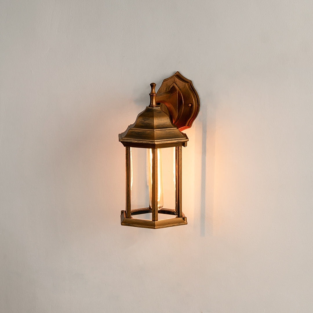 Antique brass outdoor wall light on white background featuring a clear glass lantern frame for minimal entry path decor.