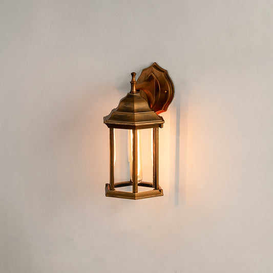 Antique brass outdoor wall light on white background featuring a clear glass lantern frame for minimal entry path decor.