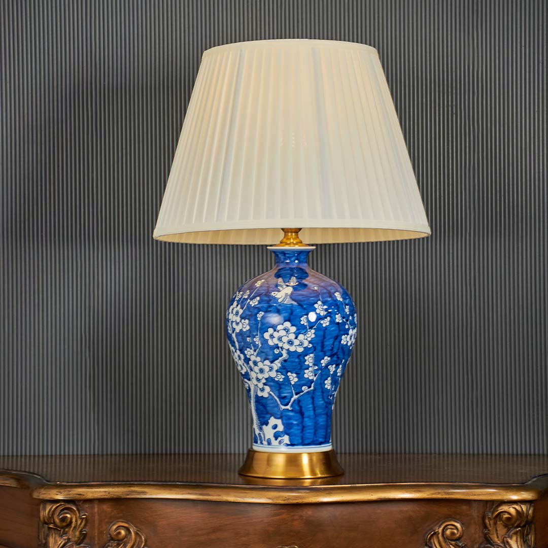 Blue ceramic floral table lamp with warm cream shade highlighted on a dark background creating an elegant classic decor look.