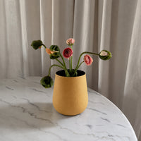 Yellow textured metal vase with colorful flowers on marble table for bright cozy modern home interior decor styling.
