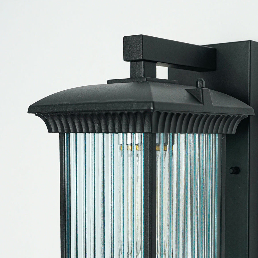 Close view of black metal outdoor wall light with ribbed glass shade showcasing durable weather resistant exterior lighting design.