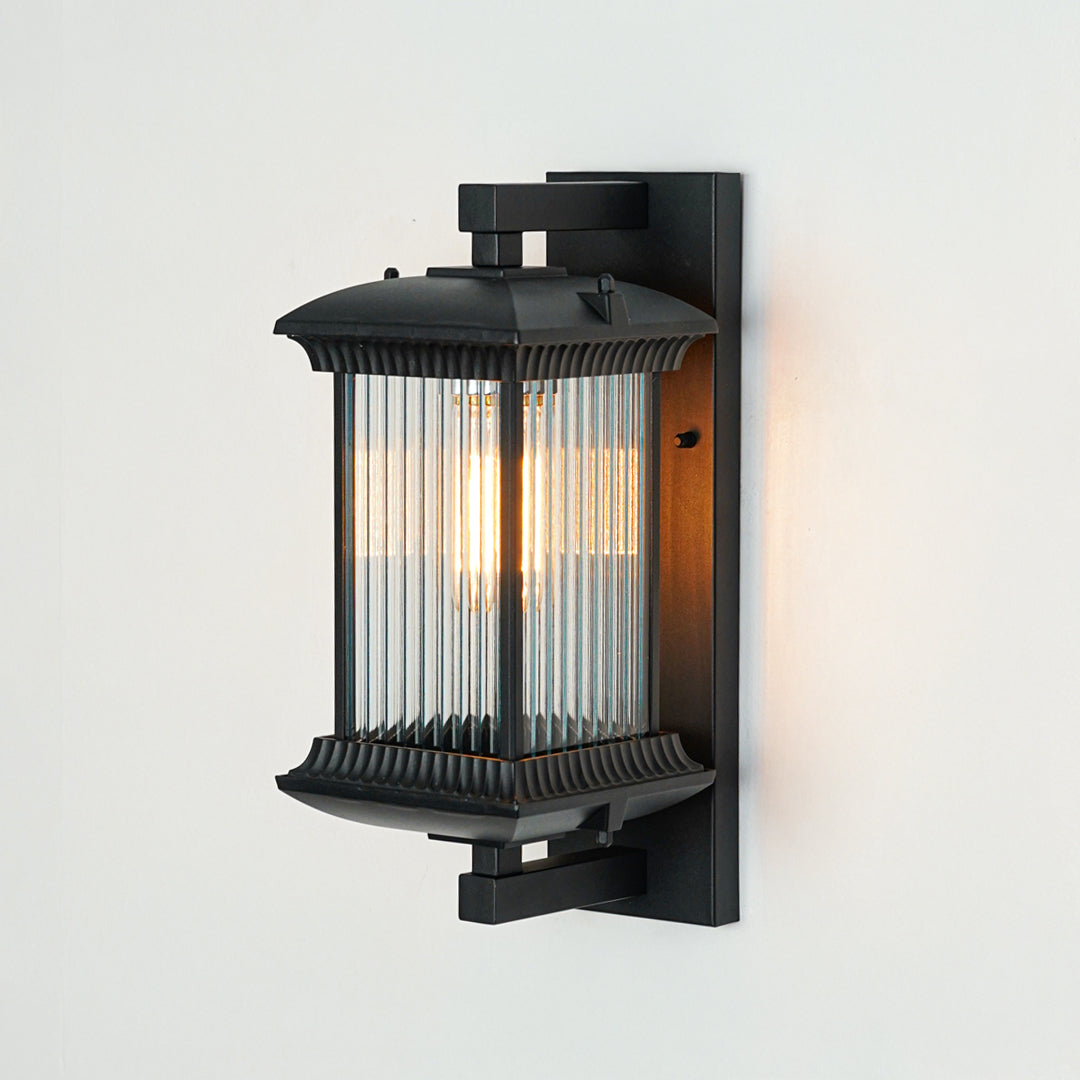 Black outdoor wall light with ribbed glass shade mounted on neutral wall background ideal for exterior porch or entry lighting.