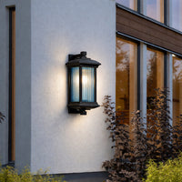 Black outdoor wall lantern with clear glass panels mounted beside wooden door on exterior wall ideal for porch or entry lighting.
