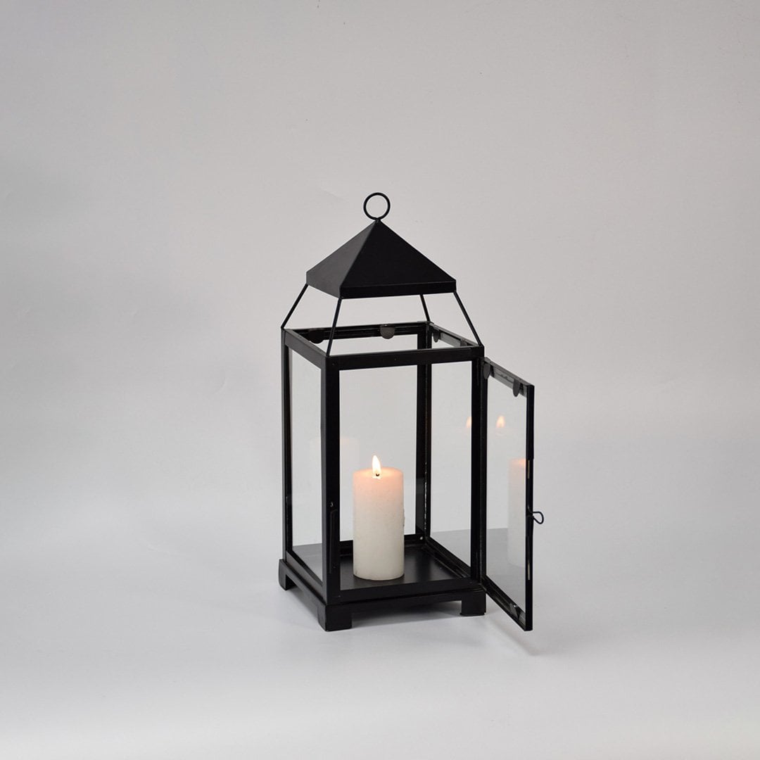 Black metal lantern displayed on white background showcasing clean lines glass panels and timeless decorative lighting design.