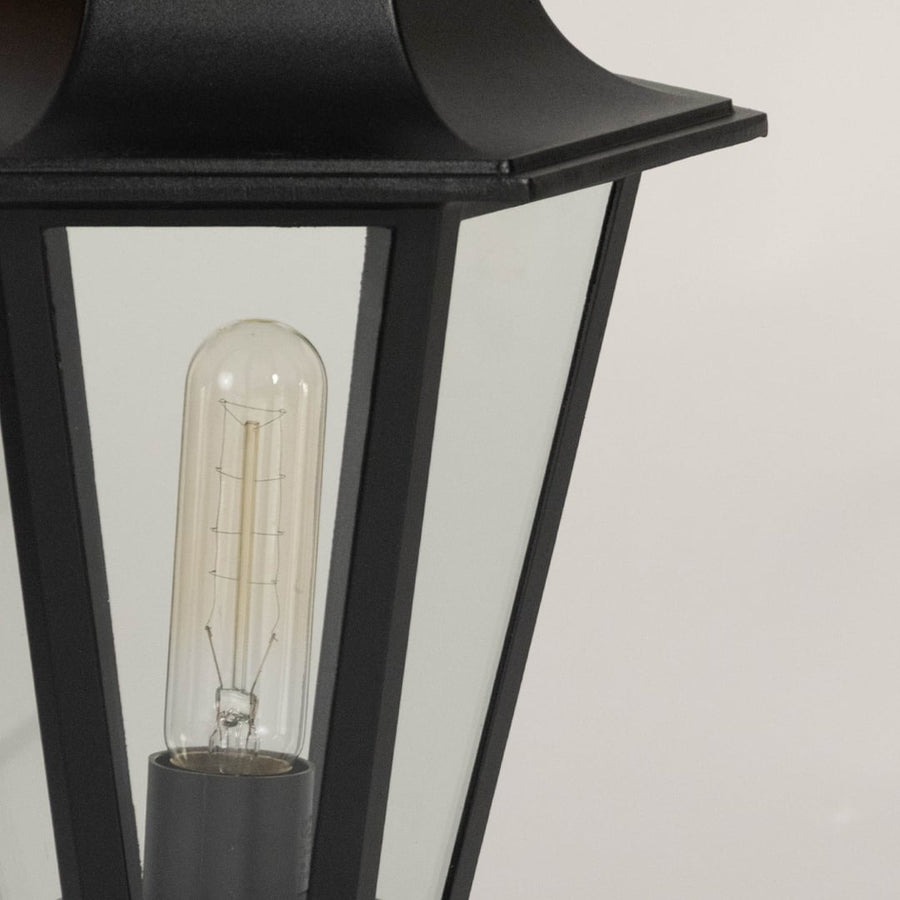 Closeup of black pillar lamp with glass shade and bulb highlighting elegant design for outdoor gate and home garden lighting.
