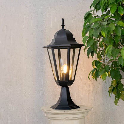 Black pillar lamp glowing warmly on stone pillar for outdoor gate and garden pathway lighting with stylish home entrance decor.