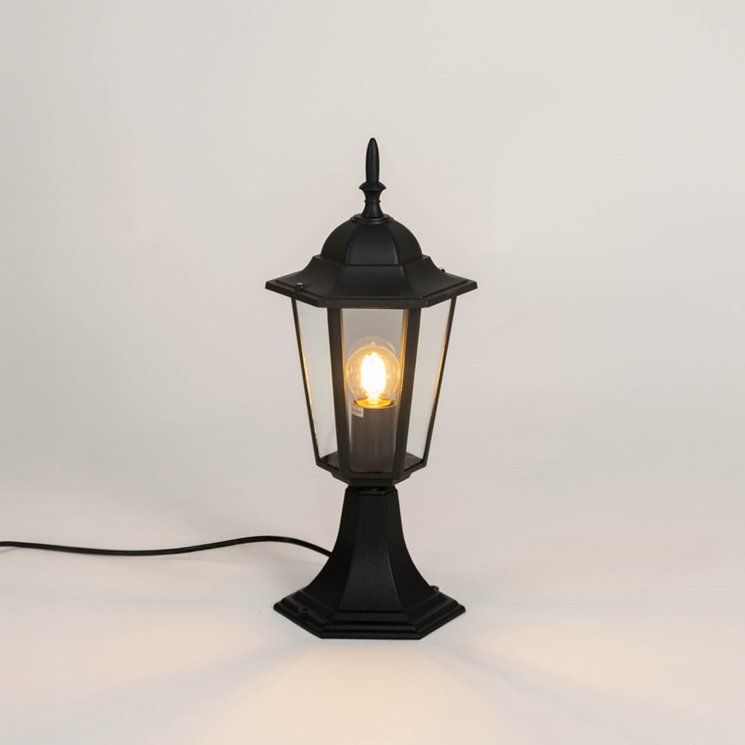 Black outdoor gate light with warm glowing bulb and clear glass shade for elegant exterior decor use.