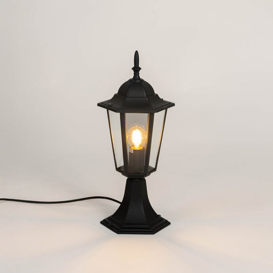 Black outdoor gate light with warm glowing bulb and clear glass shade for elegant exterior decor use.