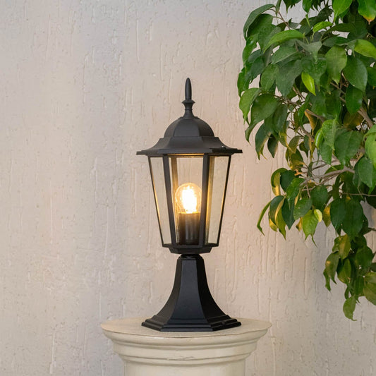 Black pillar lamp glowing warmly on stone pillar for outdoor entrance and garden pathway lighting with stylish home design.