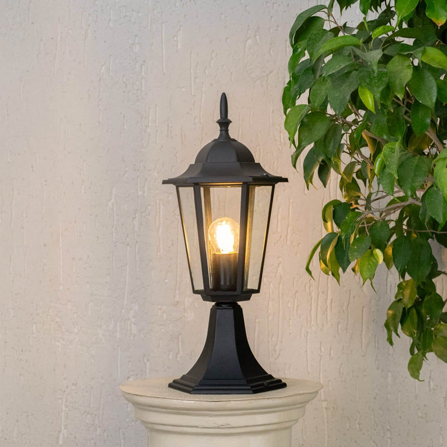 Black pillar lamp glowing warmly on stone pillar for outdoor entrance and garden pathway lighting with stylish home design.