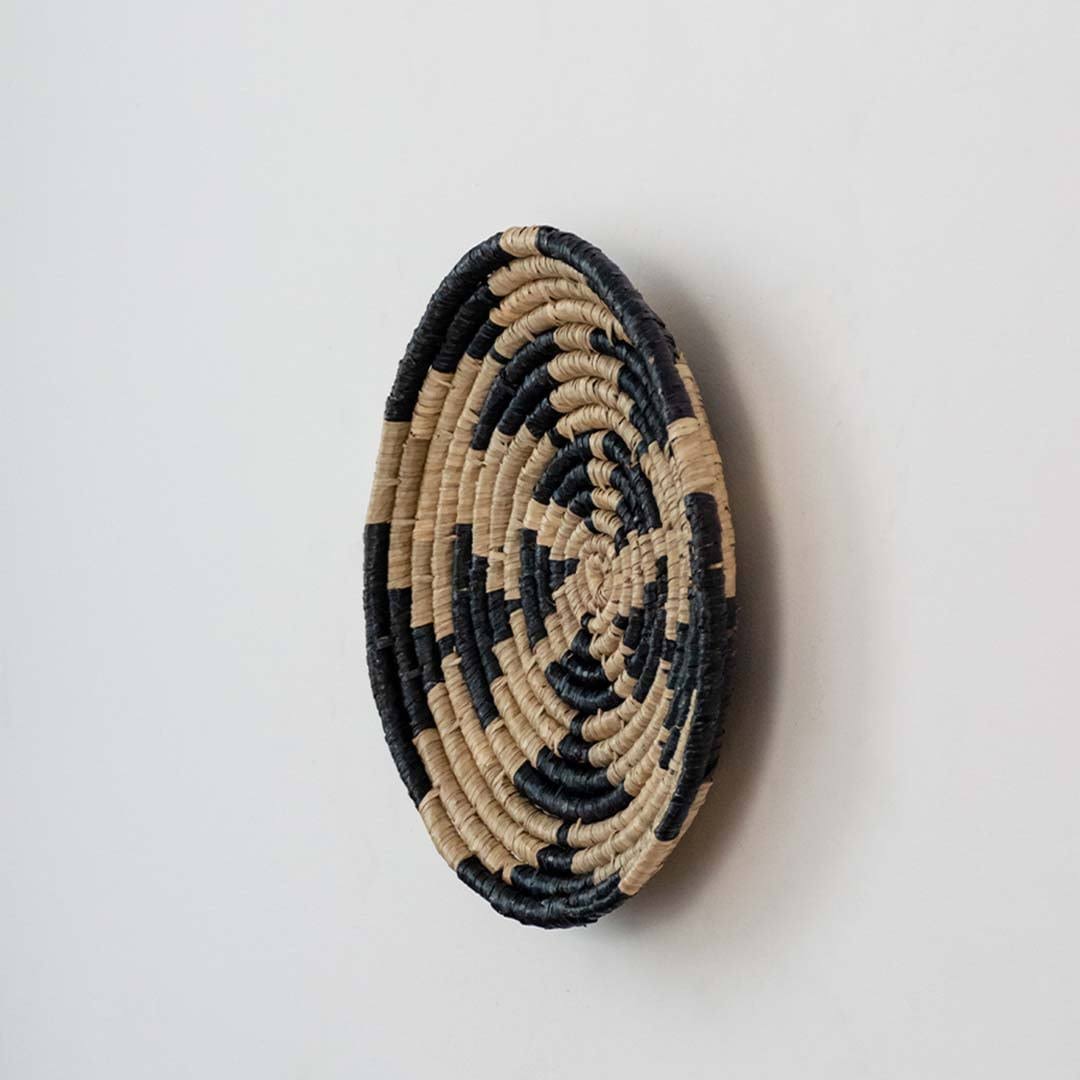 Handwoven seagrass round wall basket decor in natural beige and black with raised woven profile shown on white background.
