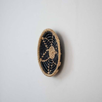 Handwoven seagrass round wall basket decor in natural beige and black with raised spiral woven profile on white background.