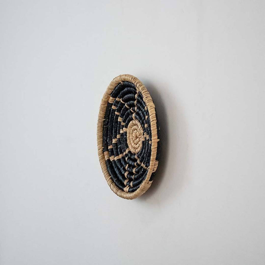 Handwoven seagrass round wall basket decor in natural beige and black with raised spiral woven profile on white background.