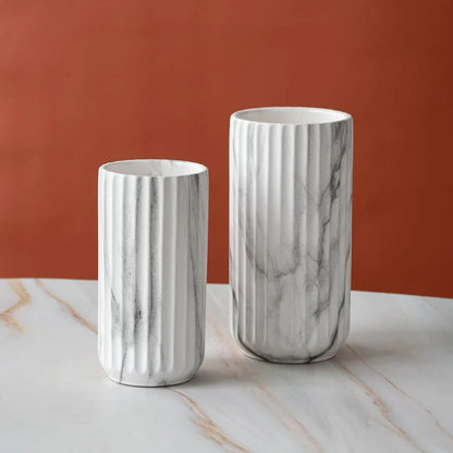 Two white fluted ceramic vases with gray marble veining, displayed on a white marble surface against a terracotta orange background.