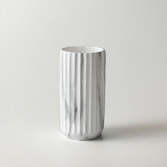 A white ceramic cylindrical cup or tumbler with vertical fluted ridges and a subtle gray marble pattern, set against a plain light gray background.