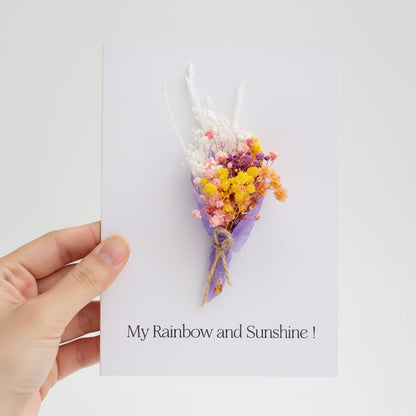 Hand holding a white greeting card featuring a colorful mini dried flower bouquet isolated on a clean white background.