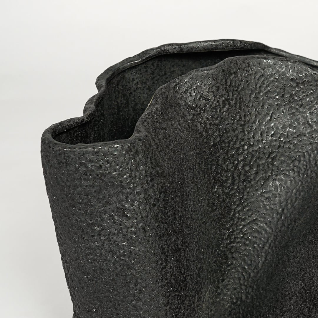 Detailed closeup of black metal decorative vase showcasing rough textured surface and abstract form.