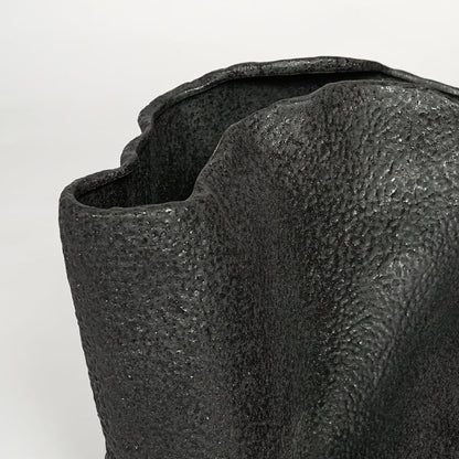 Detailed closeup of black metal decorative vase showcasing rough textured surface and abstract form.
