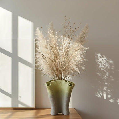 Green gradient textured ceramic decorative vase styled with dried pampas grass on wooden console in warm sunlit interior.