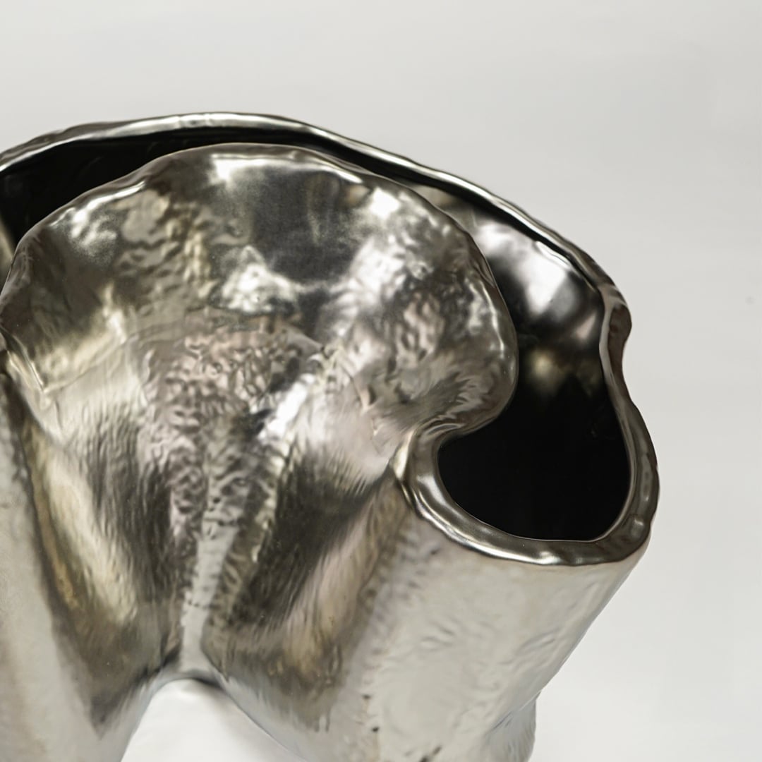 Close view of silver metal decorative vase featuring organic sculpted form and reflective polished finish.