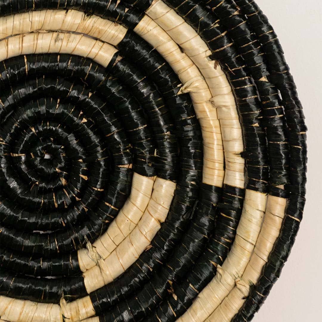 Detailed closeup of handcrafted black cream seagrass wall basket with woven concentric spiral pattern for artisan decor.