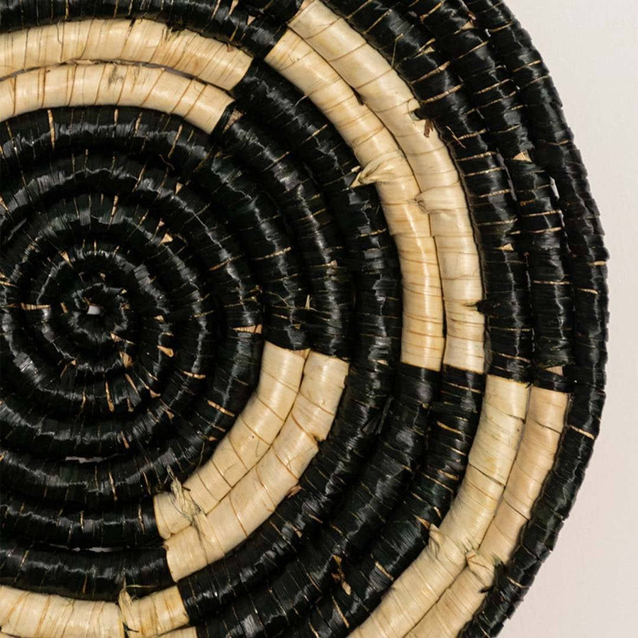 Detailed closeup of handcrafted black cream seagrass wall basket with woven concentric spiral pattern for artisan decor.