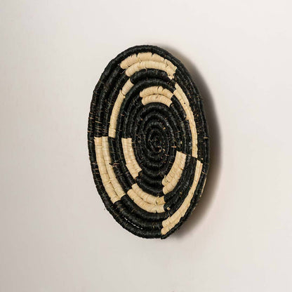 Side view of handcrafted black and cream seagrass wall basket with geometric concentric ring pattern for boho wall decor.