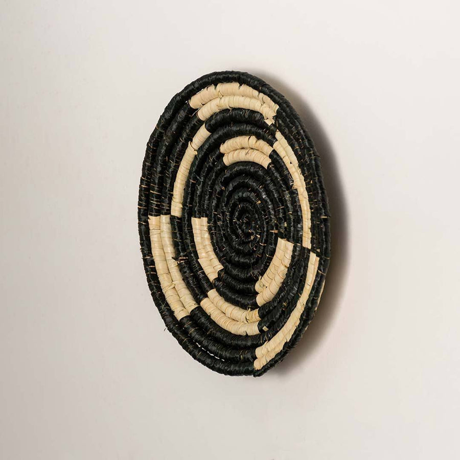 Side view of handcrafted black and cream seagrass wall basket with geometric concentric ring pattern for boho wall decor.